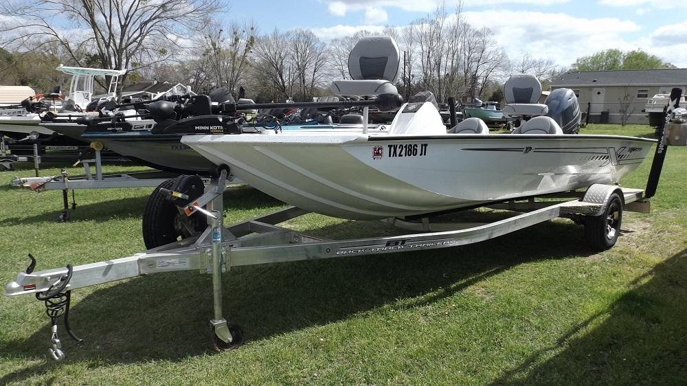 2021 Xpress XP7 white fishing boat with TX 2186 IT registration on a metallic trailer, loaded with fishing equipment and parked on grassy area at Lake Fork. Various boats and trailers in the sunny, partly cloudy background.