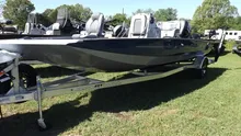 "2024 Xpress H20B boat in sleek black and silver, part of the Stainless Package, secured to a metal trailer on grassy area at Lake Fork. Surrounded by other marine equipment, boats, and trailers with trees and clear skies overhead.