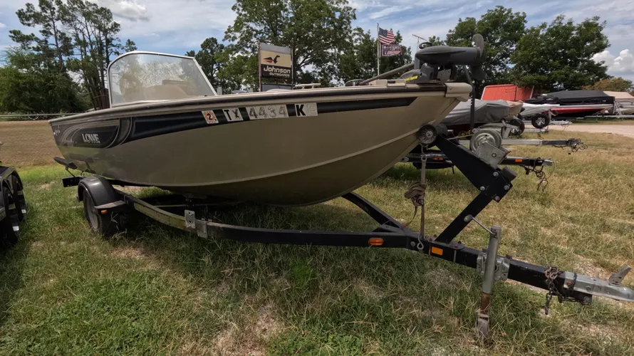 2005 Lowe Fish-Ski FS175 fishing boat on a trailer at Lake Fork with registration numbers displayed. Tan 17' boat with black accents, surrounded by trees and an American flag in the background.