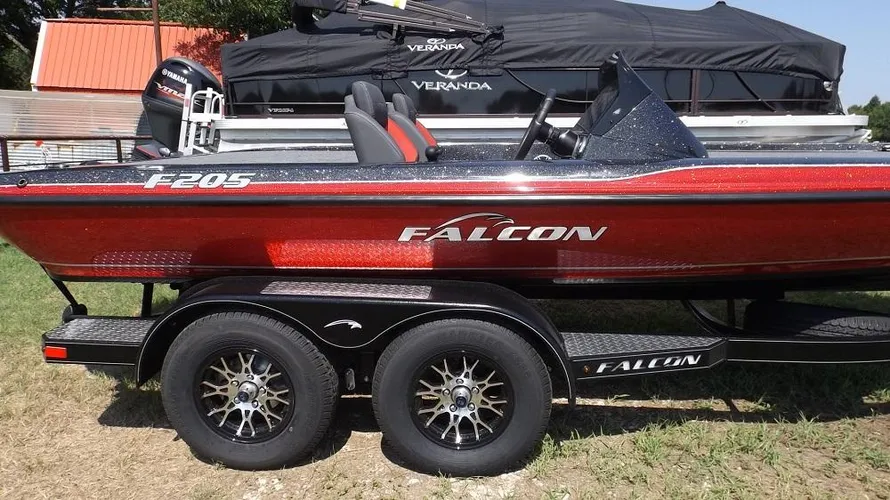 Red 2025 Falcon F205 boat on dual-axle trailer with stylish rims at Lake Fork; showcases sleek detailing, visible cockpit area with seats. Background features a covered Veranda boat.