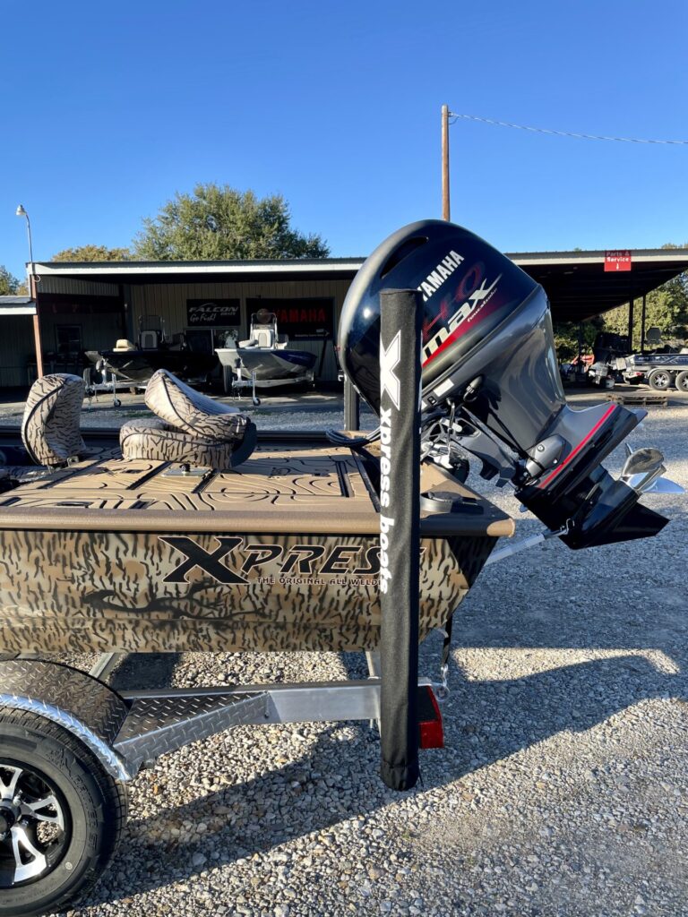 Camo-patterned Xpress Xplorer boat with Yamaha 90 outboard motor on trailer at Sartin Marine, Lake Fork. Metal-roofed shelter showcasing boats and marine equipment in the background.