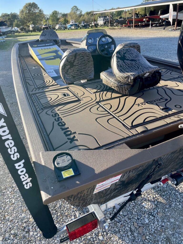 Camouflage-themed Xpress Xplorer fishing boat with Yamaha 90 at Sartin Marine, Lake Fork. Central console gauges and "Xpress boats" label showcased, parked on a trailer among other marine equipment.
