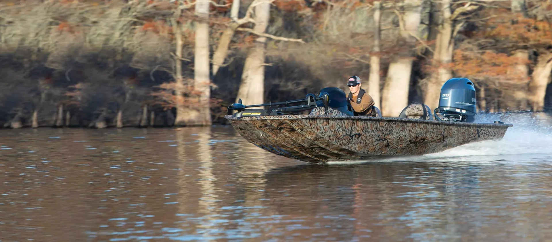 Xpress aluminum bass boat with a Yamaha 90 running past flooded cypress timber